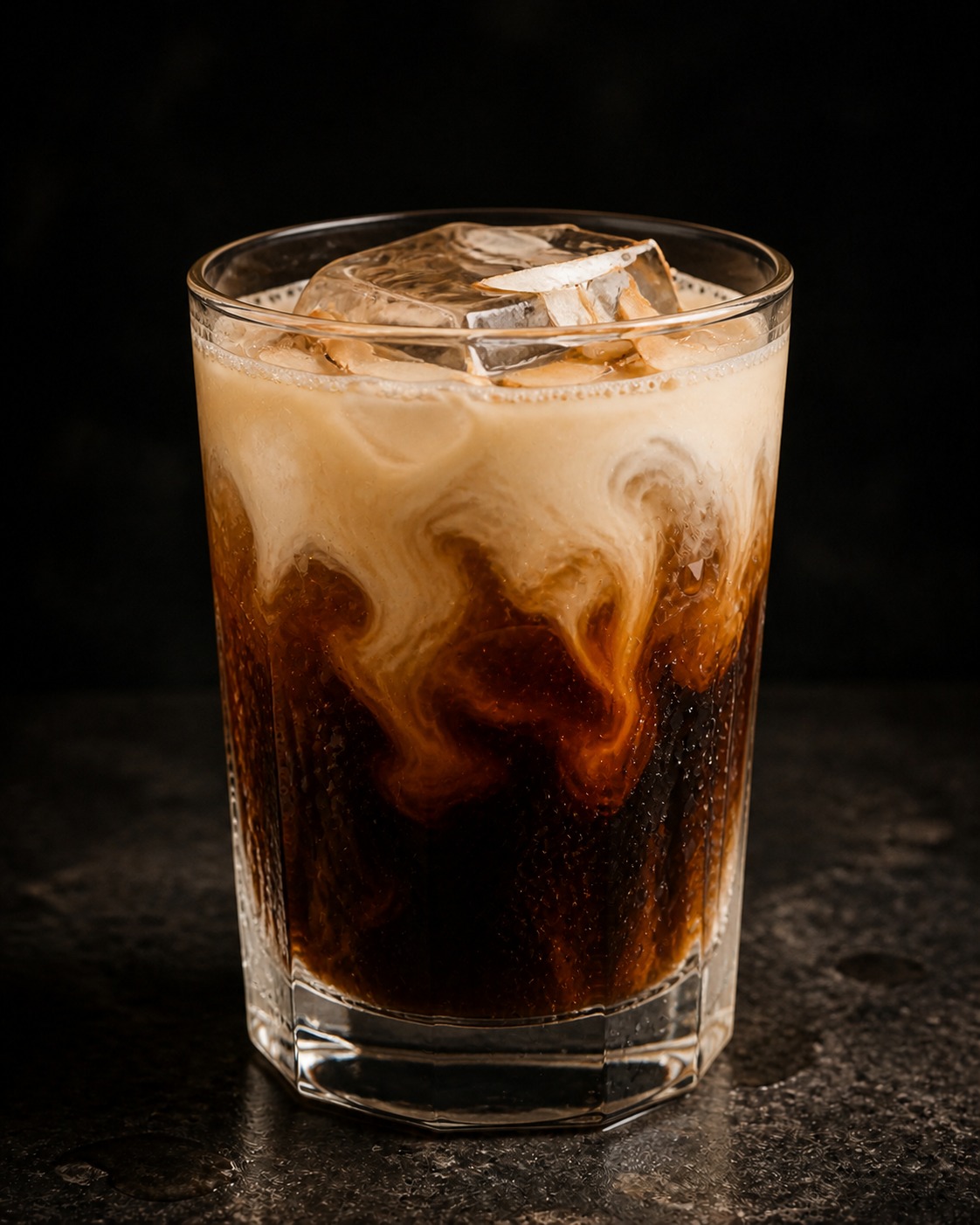 Rocks glass of coffee cocktail with coconut cream swirling through dark coffee over ice