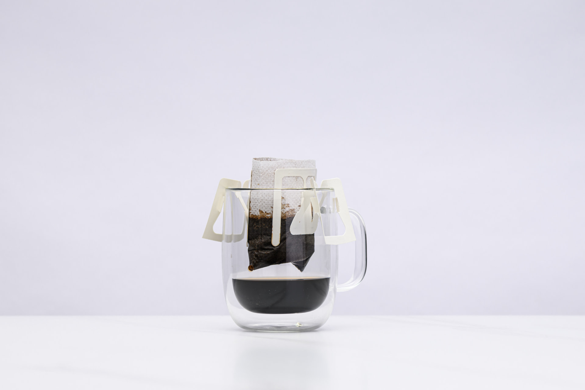 A Sampan drip bag suspended over a glass mug as brewed coffee drips through and collects below