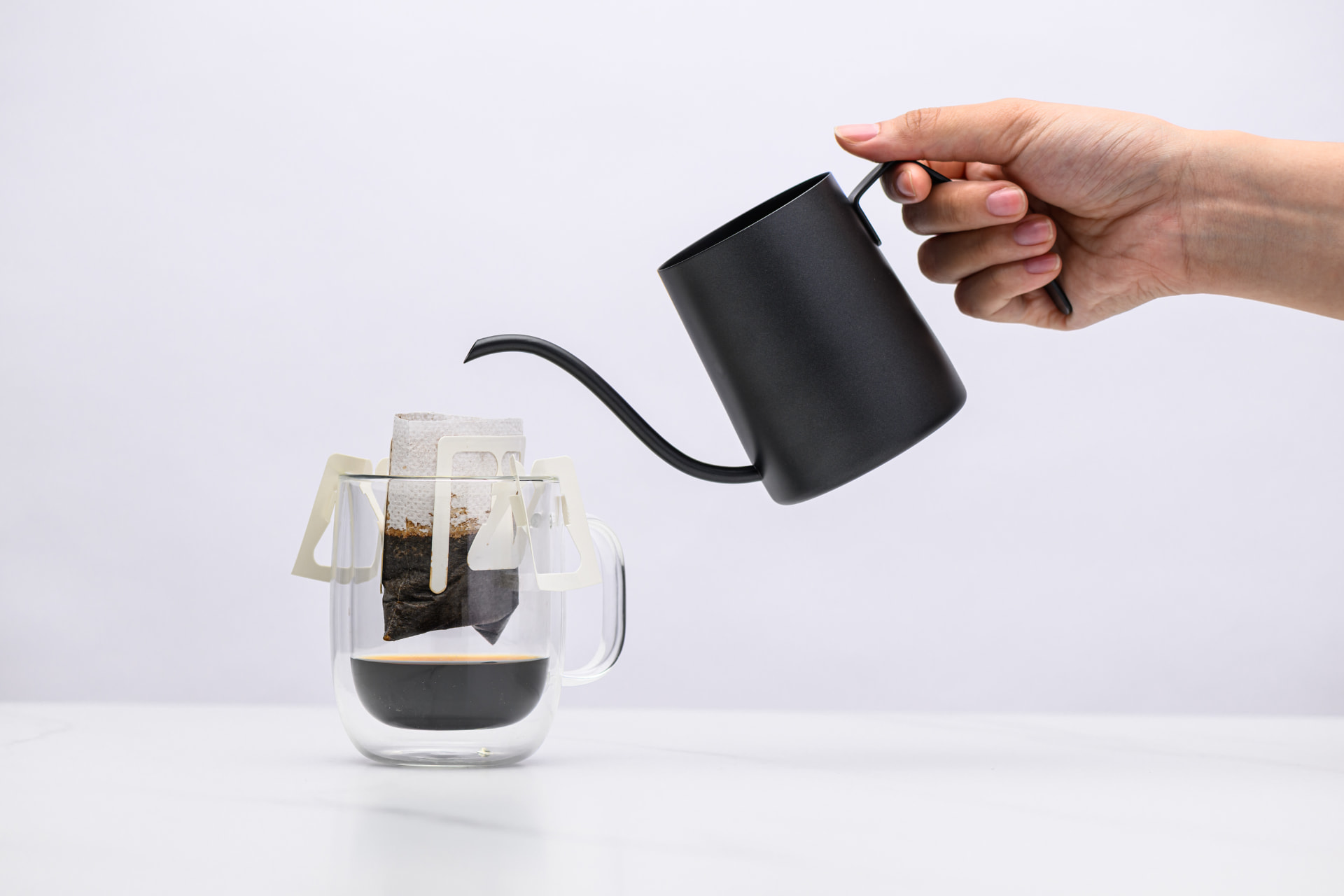 Hot water being poured from a black gooseneck kettle into a Sampan drip bag resting on a glass mug